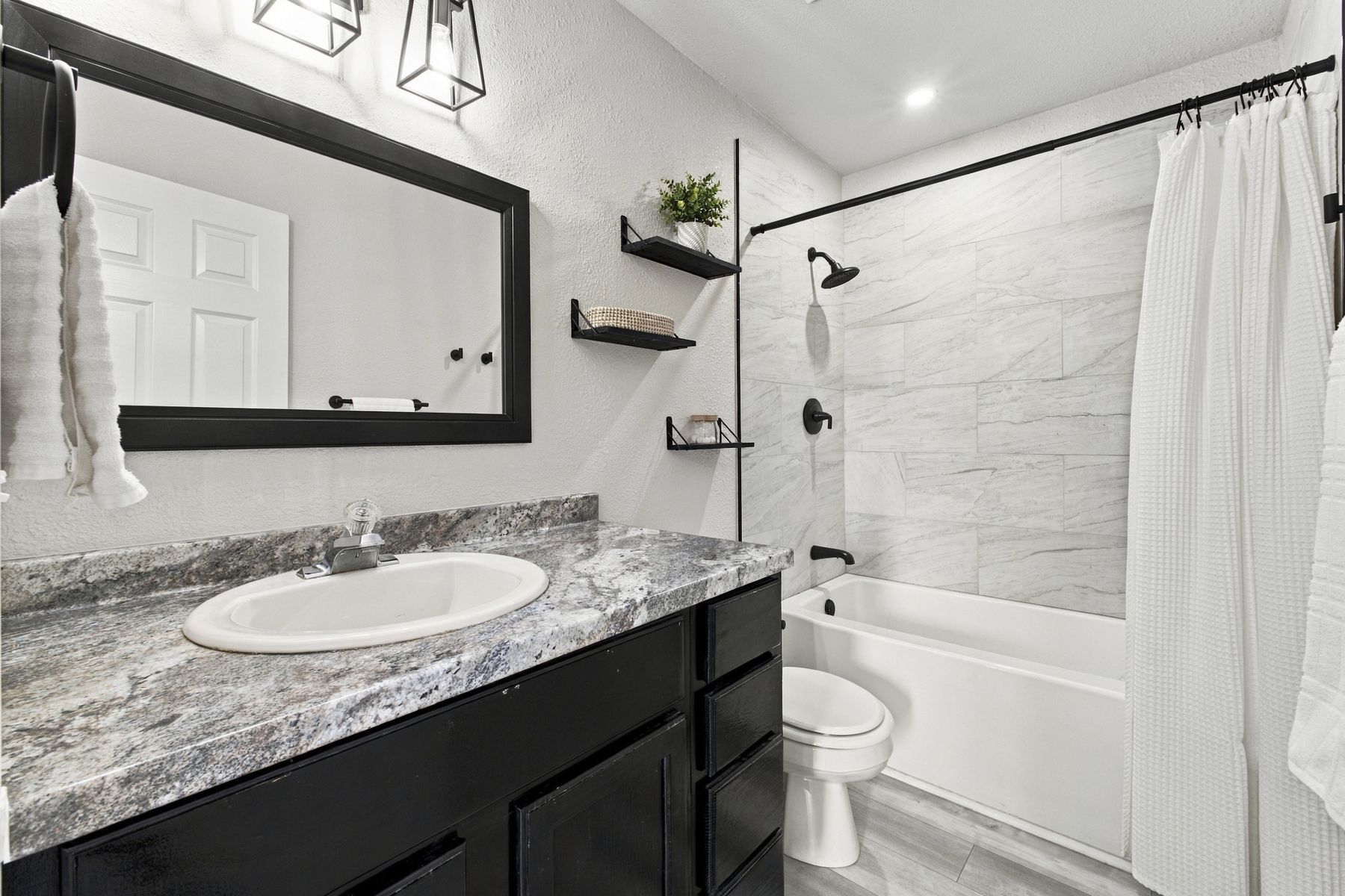 Unit A bathroom with dark vanity and tiled tub surround