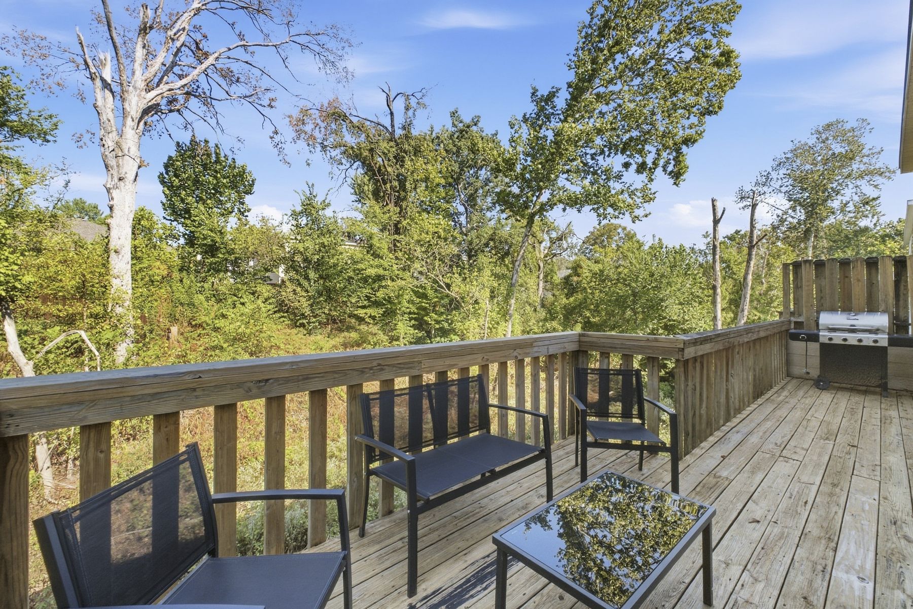 Unit A rear deck with seating and gas grill, backing to the woods